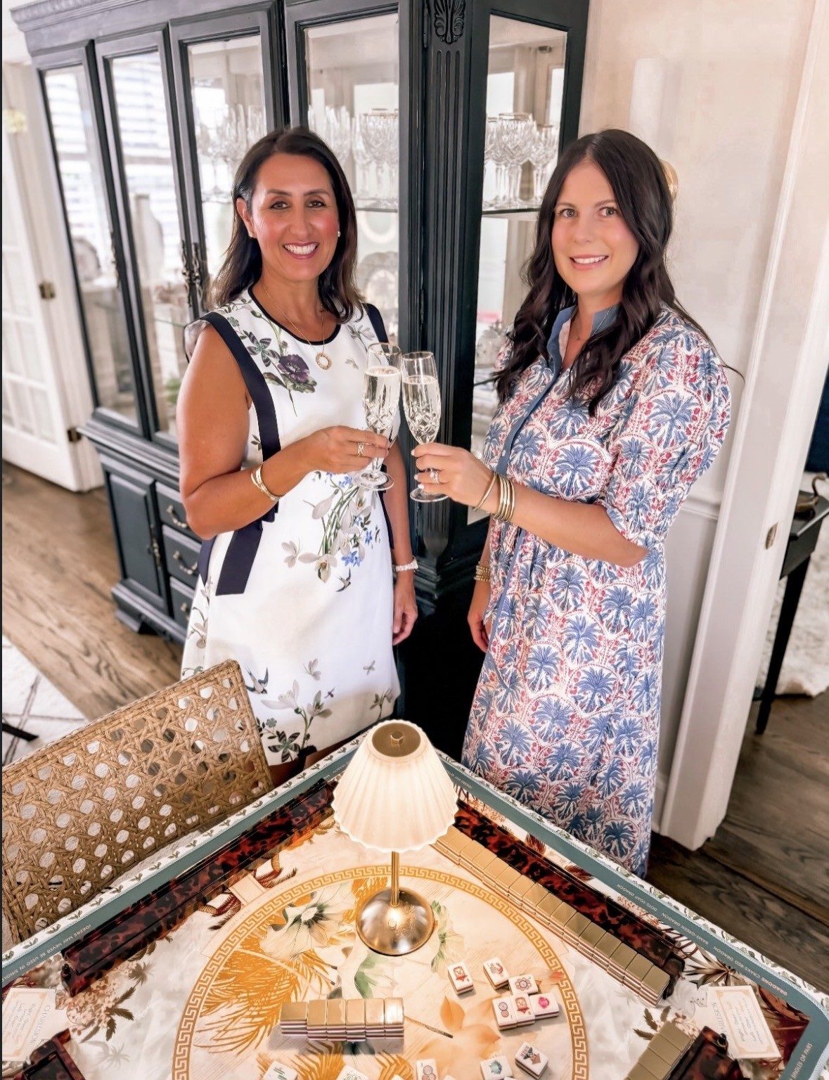 Ana and Meg toasting with champagne beside a set mahjong table