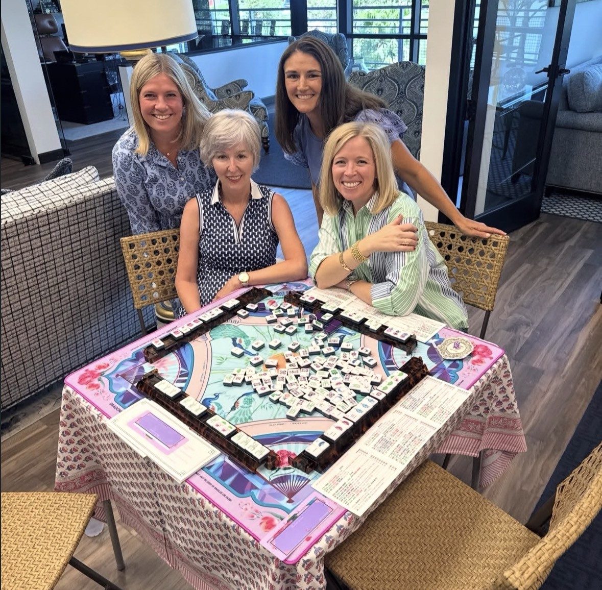Four friends smiling around a colorful mahjong table mid game