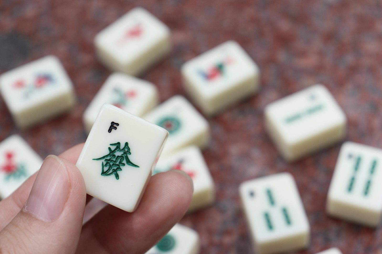 Close up of a hand holding a mahjong tile above the table